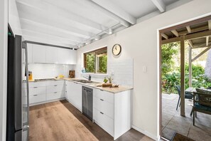 A modern kitchen with white cabinetry, a built-in dishwasher, and a window overlooking a garden. - Forest View Retreat Margaret River (Margaret River)
