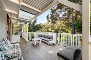 A covered outdoor area with a wooden deck, white railings, and a grey sofa with cushions. - Forest View Retreat Margaret River (Margaret River)