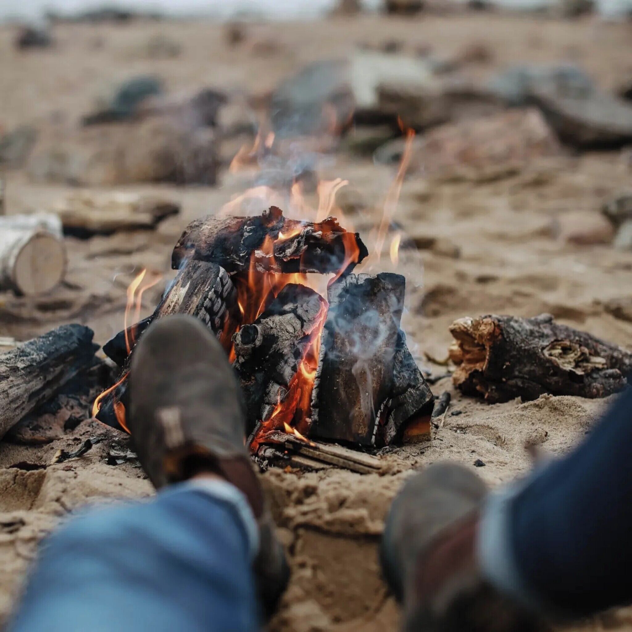 A campfire with logs and flames, surrounded by sand.