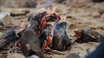 A campfire with logs and flames, surrounded by sand.