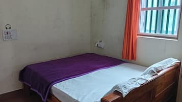 Una cama individual con una manta morada, una sábana blanca y un cabecero de madera. Hay un enchufe y una toma de corriente en la pared.