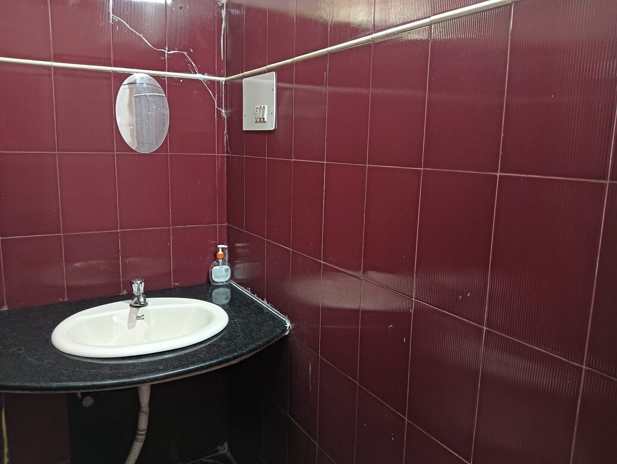 Une salle de bain avec un lavabo blanc, un miroir et un mur recouvert de carreaux rouges.