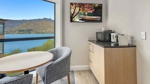 A modern room with a dining area, a kitchen, and a large window offering a view of a lake and mountains. - Lakeside Luxury for Two | Modern Oak Shore Retreat (Queenstown)