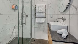 A modern bathroom with a glass-enclosed shower, a white sink, and a marble-tiled wall. - Lakeside Luxury for Two | Modern Oak Shore Retreat (Queenstown)