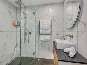 Ein modernes Badezimmer mit einer gläsernen Duschkabine, einem weißen Waschbecken und einer Wand mit Marmorfliesen.
