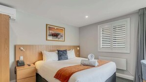 A hotel room with a bed, bedside table, and a window with shutters. - Lakeside Luxury for Two | Modern Oak Shore Retreat (Queenstown)