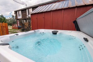 A hot tub in a backyard with a red shed and a wooden fence.