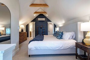 A bedroom with a bed, bedside tables, a dresser, a mirror, and a door leading to another room.