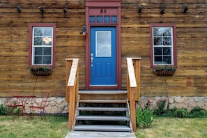 A wooden cabin with a blue door, numbered 85, and a set of wooden stairs leading to the entrance.