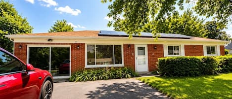 Een tweelaags huis met een garage, zonnepanelen en een rode auto ervoor geparkeerd.