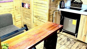 Un intérieur en bois avec une table en bois, un banc, un réfrigérateur, une bouilloire et une petite décoration en forme de maison.