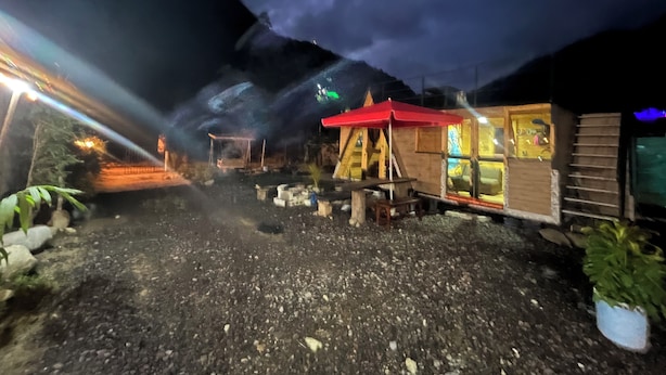 Une construction rustique en bois, avec un toit rouge, qui pourrait être une cabane ou un petit bâtiment, se dressant sur fond de montagnes.