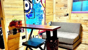 Une pièce avec un plancher en bois, une table avec une chaise, un canapé et un tableau abstrait aux couleurs vives accroché au mur.