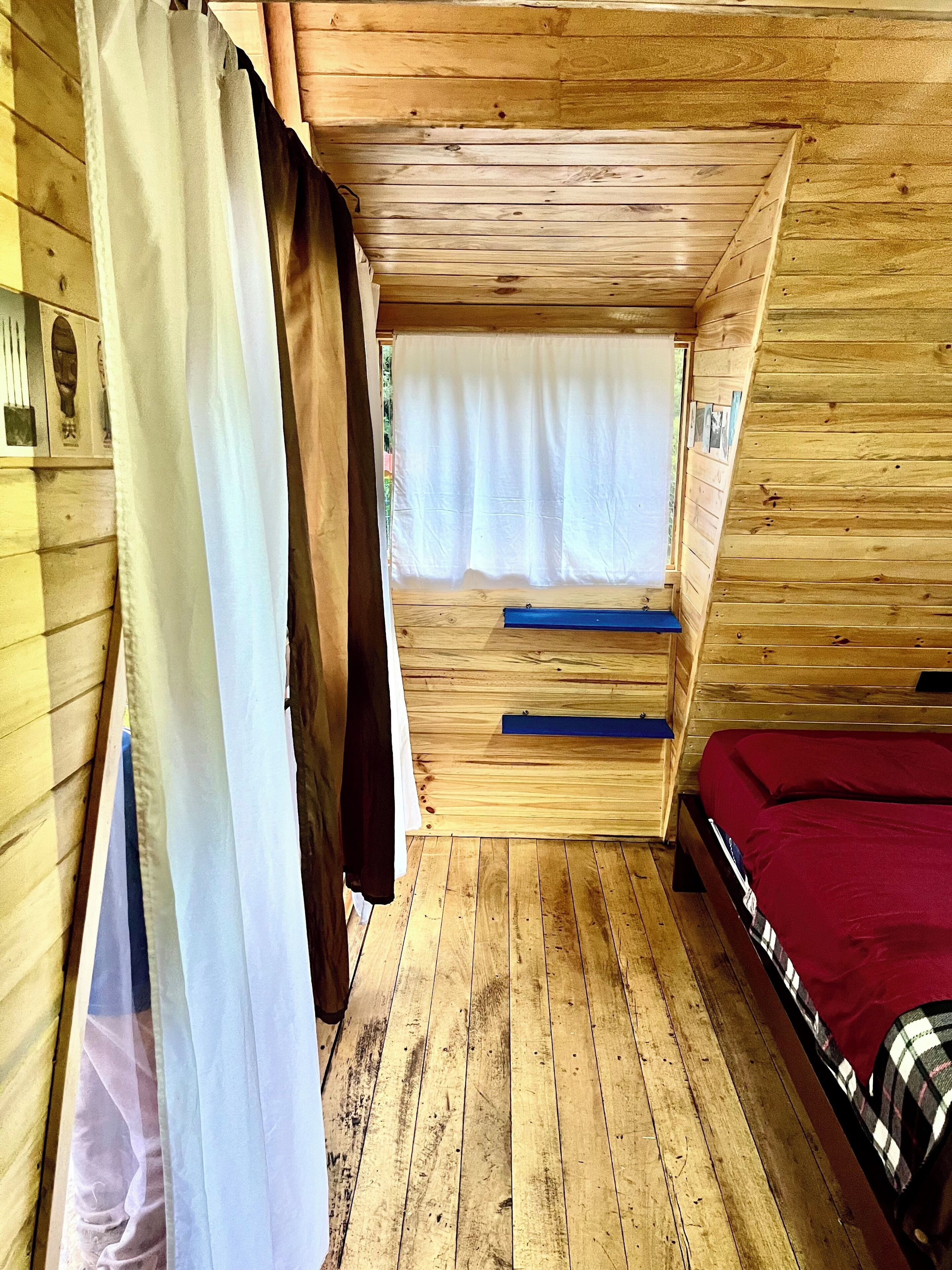 A wooden interior with a bed, a window with curtains, and a wooden floor.