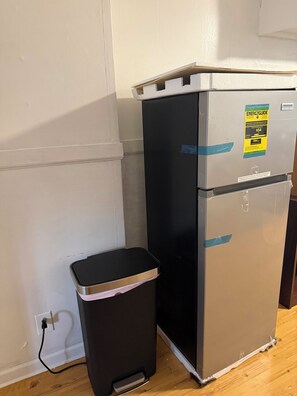 Ein kompakter Kühlschrank mit Energiesparaufkleber neben einer schwarzen Mülltonne.