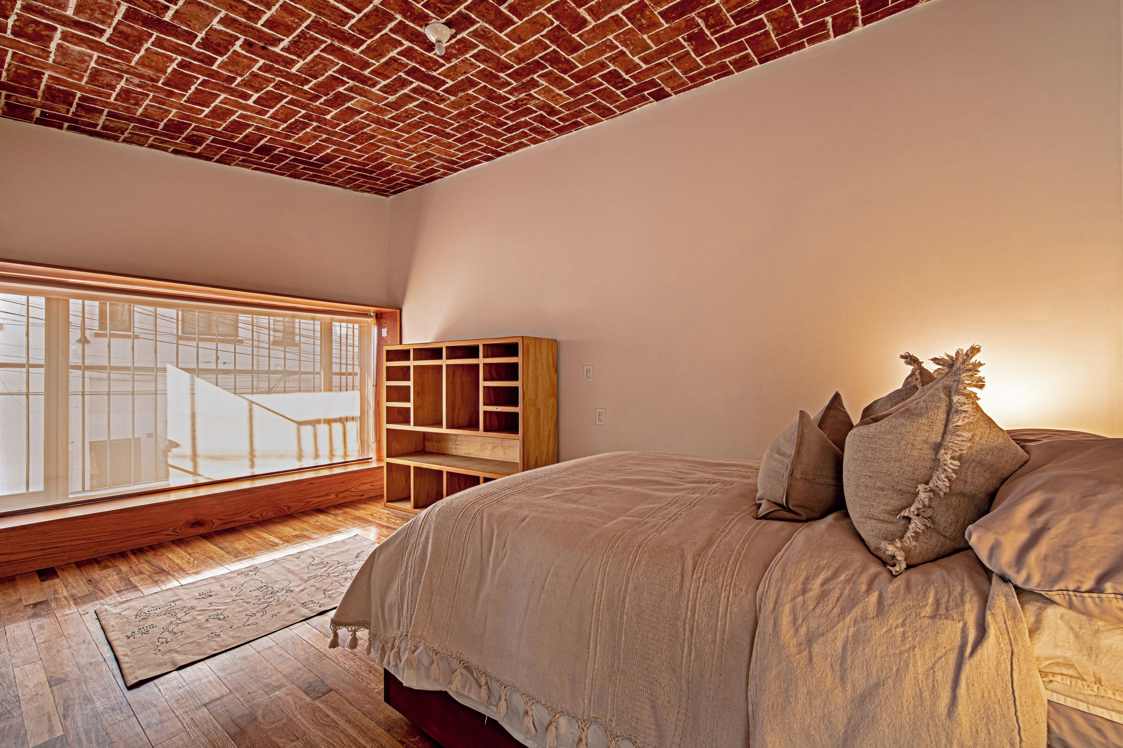 A bedroom with a large bed, a wooden bookshelf, a window with a view, and a brick ceiling.