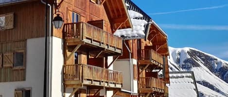 A wooden chalet with multiple balconies and a mountain backdrop.