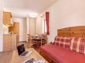 A compact room with a wooden sofa, a dining table with chairs, a laptop on a table, and a kitchenette with wooden cabinets. - Les Fermes de Saint Sorlin by Interhome (Saint Sorlin d'Arves)