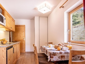 A compact kitchen with wooden cabinets, a microwave, and a dining area with a table set for breakfast. - Les Fermes de Saint Sorlin by Interhome (Saint Sorlin d'Arves)