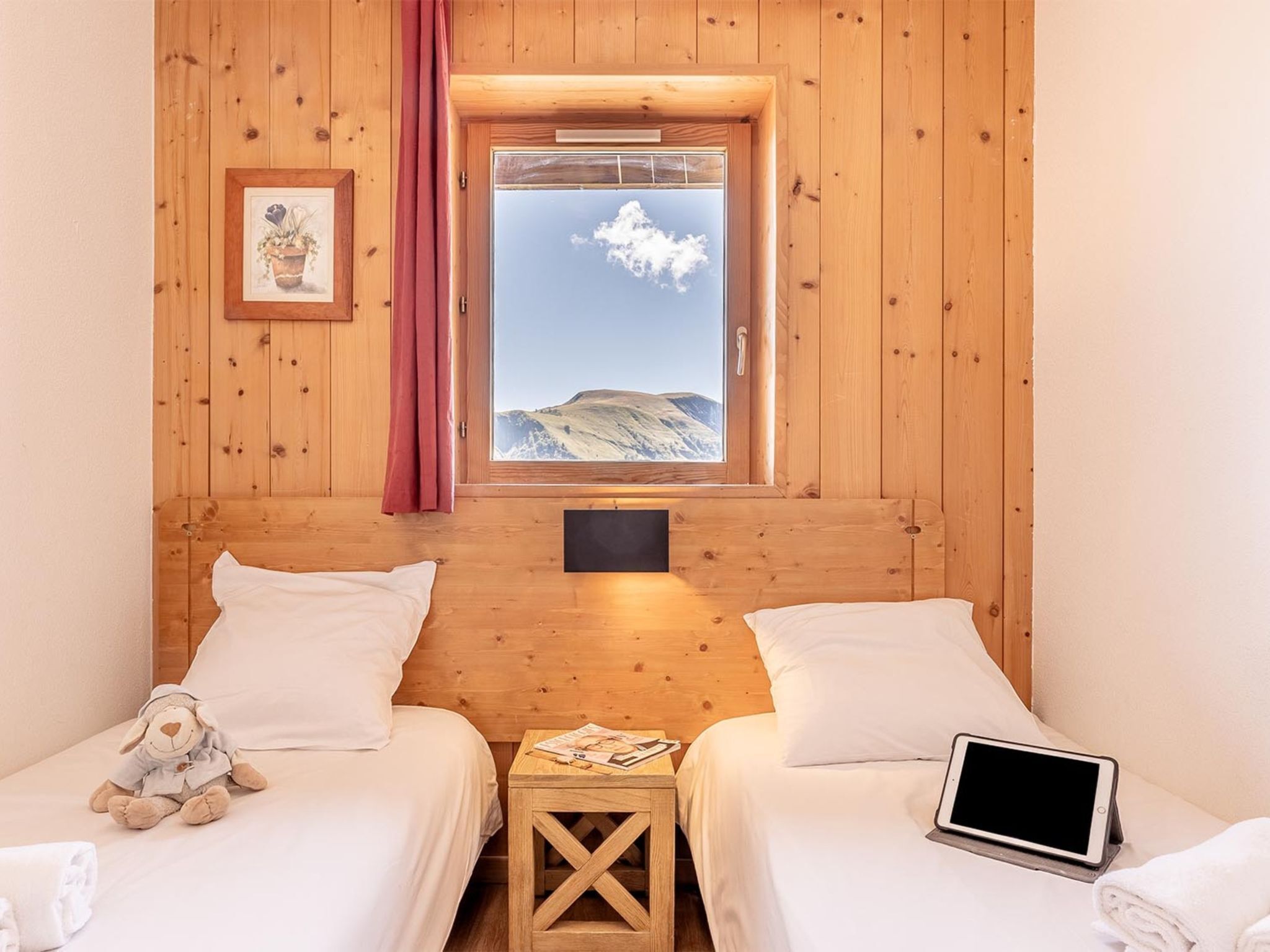 Een kamer met twee bedden, een raam met uitzicht op een berg, een kleine tafel met een lamp en een knuffel op een van de bedden.