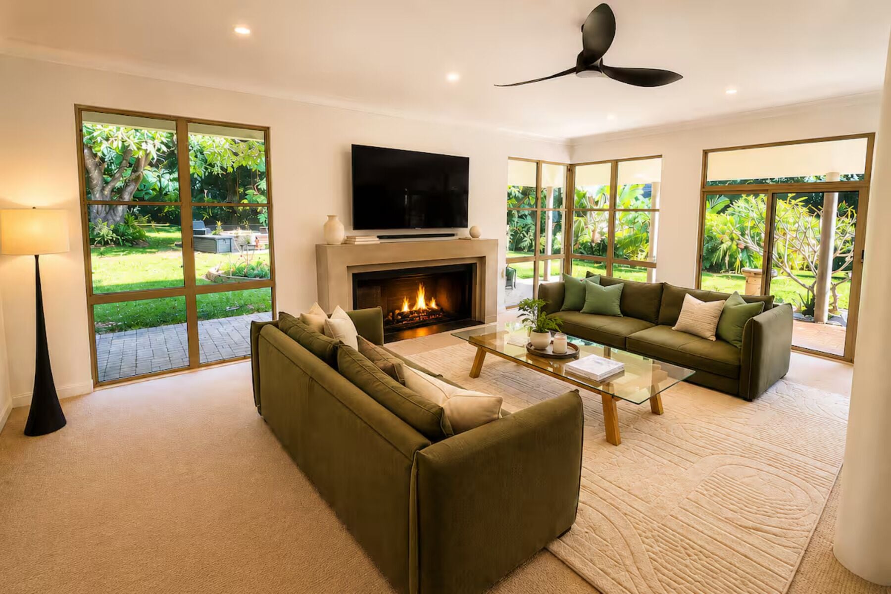 A modern living room with a fireplace, a flat-screen TV, and a ceiling fan.