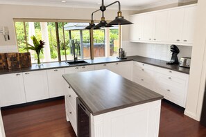 Une cuisine moderne avec des meubles blancs, un grand îlot central et une vue sur la verdure environnante.