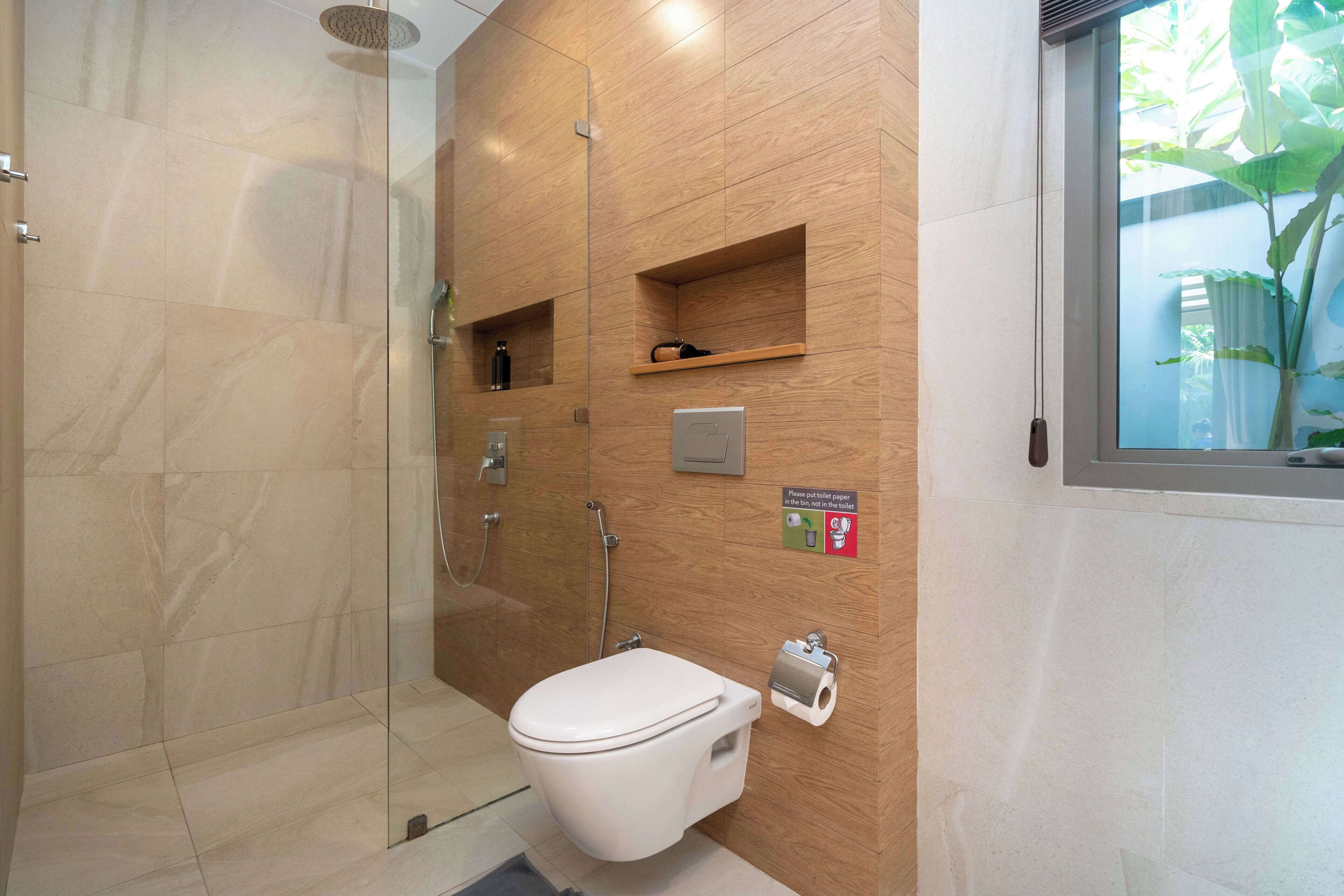 Un baño moderno con cabina de ducha de vidrio, inodoro y un estante pequeño con artículos de aseo.