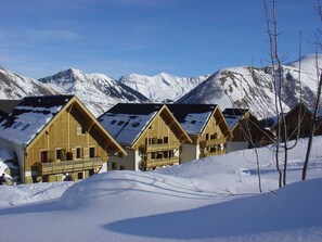A row of wooden chalets with balconies, set against a backdrop of snow-covered mountains. - Les Fermes de Saint Sorlin by Interhome (Saint Sorlin d'Arves)