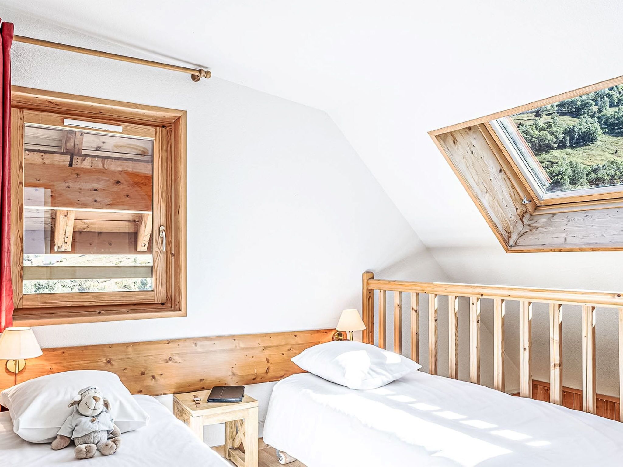 A bedroom with a wooden headboard, a bed with white bedding, a nightstand with a lamp and a stuffed toy, and a window with a view of greenery.