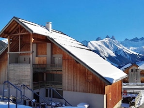 Eine Holzhütte mit Balkon vor einer schneebedeckten Berglandschaft.