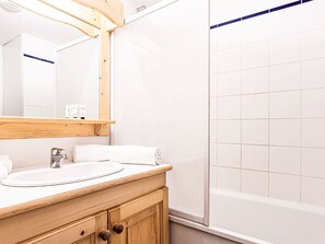 Ein Badezimmer mit einem Holzmöbel zur Aufbewahrung, einem weißen Waschbecken, einem Spiegel und einer Duschkabine.