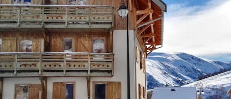 Un edificio de madera de varios pisos con balcones, un paisaje nevado y una montaña al fondo.