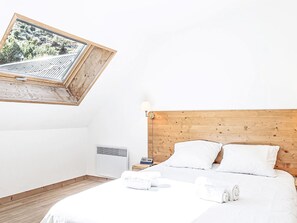 Une chambre à coucher avec une tête de lit en bois, un lit recouvert de draps blancs, une table de chevet avec une lampe et une fenêtre donnant sur un paysage verdoyant.