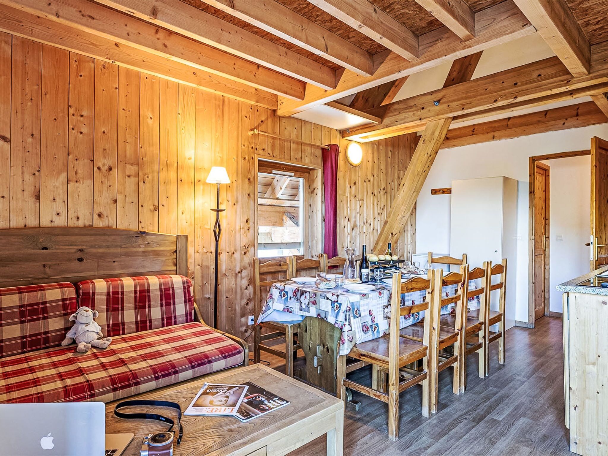 A cozy cabin interior with a dining area, wooden walls, and a sofa with a plaid blanket.