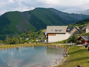 Une propriété située au bord d’un lac, comprenant un grand bâtiment, un chalet en bois et un paysage montagneux en toile de fond.
