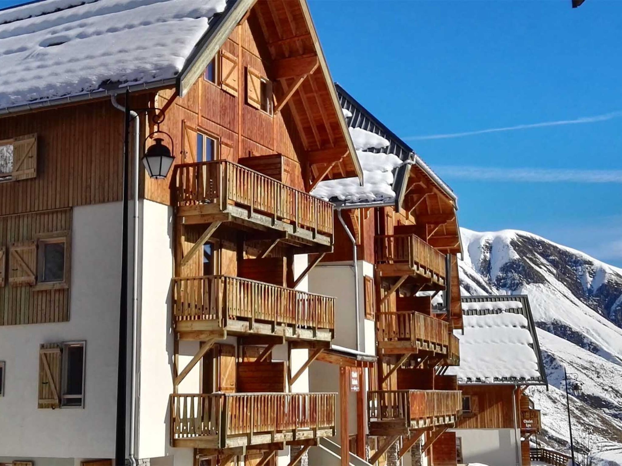 A wooden chalet with multiple balconies and a mountain backdrop.