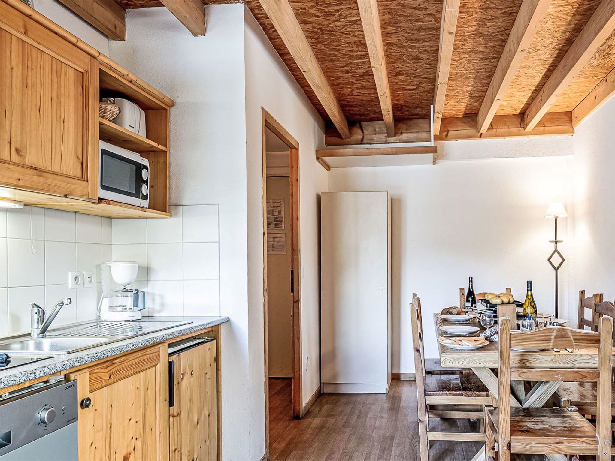 Une cuisine dotée de meubles en bois, d’un four à micro-ondes, d’une machine à café et d’un coin repas avec une table mise pour deux personnes.