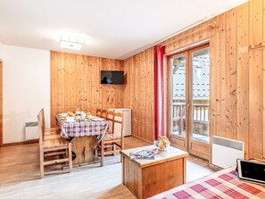 Une pièce aux murs lambrissés, avec une table à manger dressée pour quatre personnes, une petite kitchenette et une porte-fenêtre coulissante donnant sur un espace extérieur.