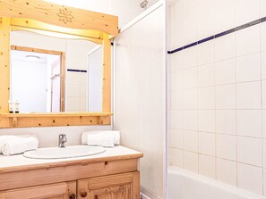 Ein Badezimmer mit einem Holzkosmetikschrank, einem Waschbecken, einem Spiegel und einer Duschkabine.