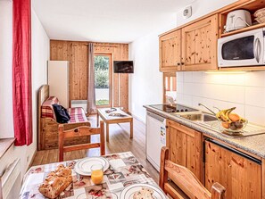 Eine kompakte Küche mit Holzausstattung, einer eingebauten Mikrowelle und einem Essbereich mit Tisch für zwei Personen.