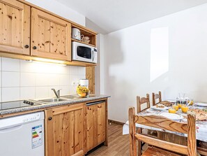 A kitchen with wooden cabinets, a microwave, a dishwasher, and a dining table set with breakfast. - Les Fermes de Saint Sorlin by Interhome (Saint Sorlin d'Arves)