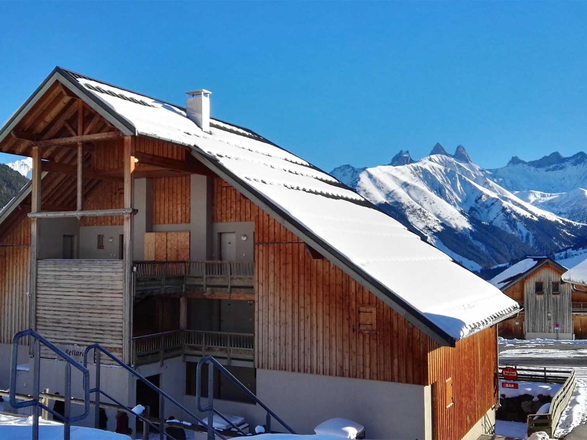 Una cabaña de madera con balcón, con montañas nevadas de fondo.