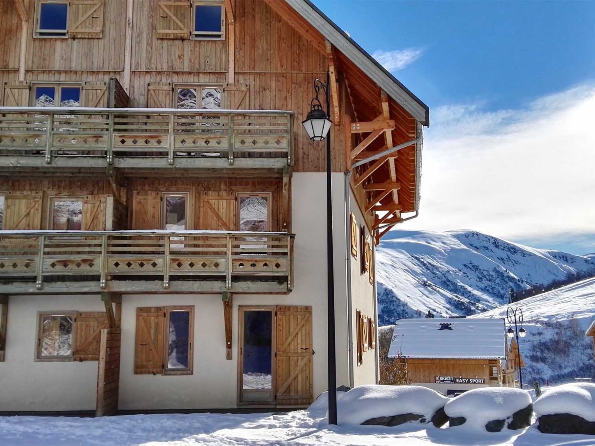 A multi-story wooden building with balconies, a snow-covered landscape, and a mountain in the background.