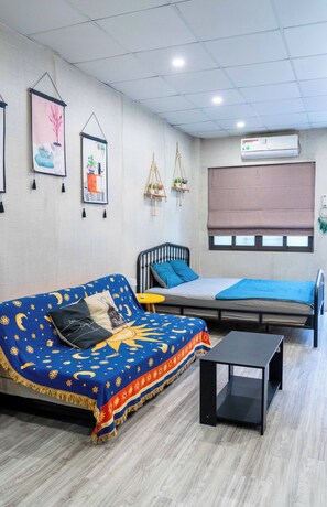 Een kamer met een bed, een bank, een kleine tafel en decoratie aan de muur, waaronder ingelijste foto's en een macramé plantenhouder.