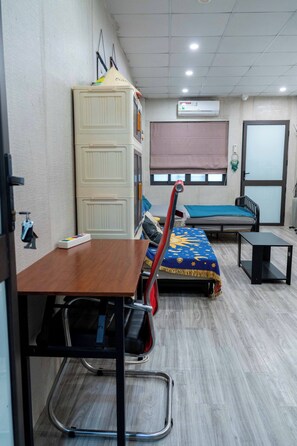 Ein Zimmer mit einem Bett, einem Schreibtisch, einem Stuhl, einem Kleiderschrank und einem Fenster mit Jalousien.