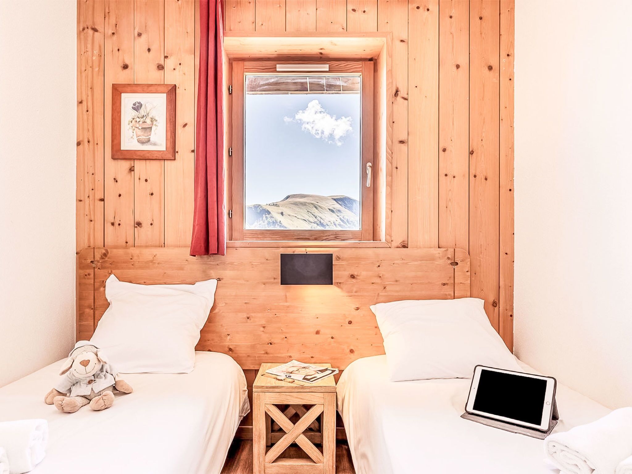 Una habitación de madera con dos camas, una ventana que ofrece vistas a la montaña, una mesita y un ordenador portátil sobre una de las camas.