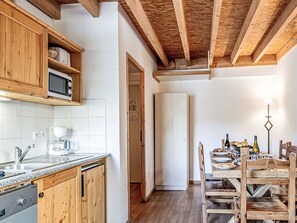 A kitchen with wooden cabinets, a microwave, a coffee maker, and a dining area with a table set for two. - Les Fermes de Saint Sorlin by Interhome (Saint Sorlin d'Arves)