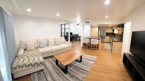 A modern living room with a sofa, coffee table, and TV. There is a kitchen area with a refrigerator and a dining table. - Renovated 1-bedroom condo in Anaheim, perfect for your stay-5 miles from Disney! (Anaheim)