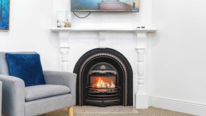 Ein Wohnzimmer mit Kamin, einem grauen Sofa und einem Fernseher, der über dem Kamin angebracht ist.