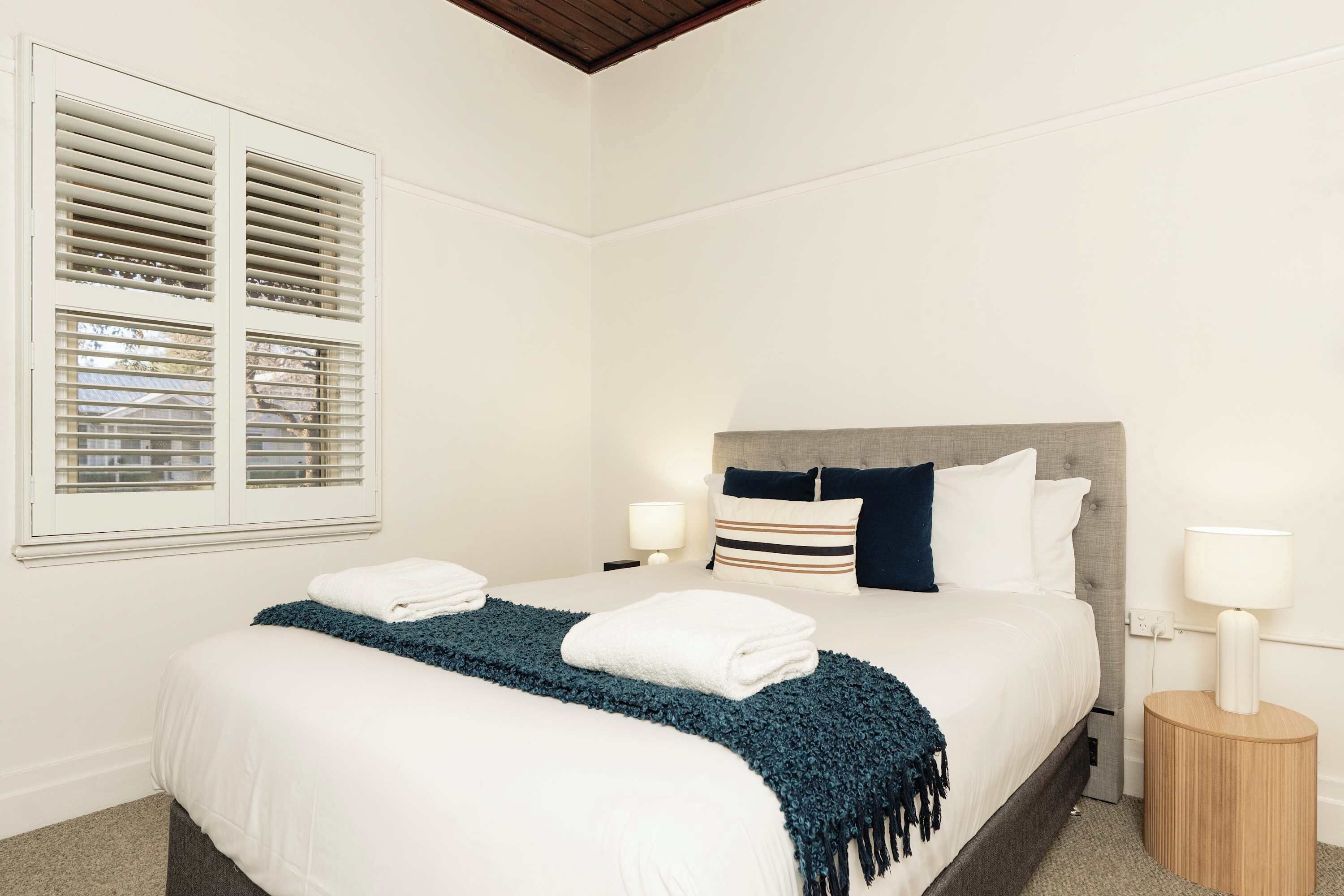 A bedroom with a bed, bedside lamps, a window with blinds, and a headboard.
